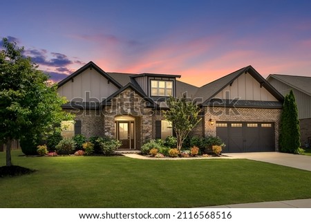 Contemporary Home Exterior with Colorful Sunset. Green Grass, Brick and Stacked Stone, Meticulous Landscaping, Warm and Inviting House. Royalty-Free Stock Photo #2116568516