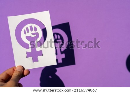 A woman holding the symbol of the fight for feminism on a purple background, clenched fist of a woman at the march protests for women's rights and equality Royalty-Free Stock Photo #2116594067