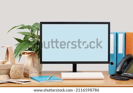 traditional modern office desk with mockup monitor screen, supplies and ip phone and buff paper bag packaging. Small business e-commerce delivery. Binders and plant. working from home. Royalty-Free Stock Photo #2116598786