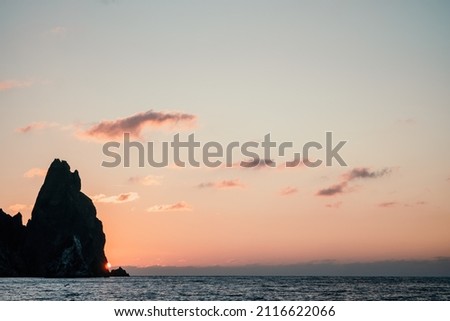 Dramatic Seascape over the beach during sunset, with rocky volcanic cliff is lit by the warm sunset. Clear sky, no clouds. Nobody. The concept of calmness silence and unity with nature. Slow motion.