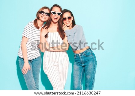 Three young beautiful smiling hipster female in trendy summer clothes.Sexy carefree women posing near blue wall in studio.Positive models in sunglasses. Cheerful and happy Royalty-Free Stock Photo #2116630247