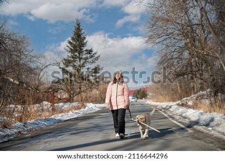 girl walks with a dog in the winter in the park. A girl in a pink jacket walks with a labrador in the park in winter. Healthy lifestyle. High quality photo