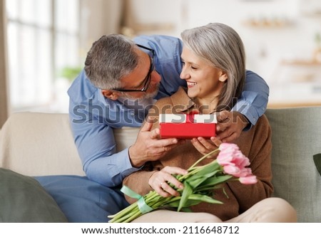 Loving senior  man husband giving  bouquet of tulip flowers and present gift box  for Valentine's day   to happy surprised wife