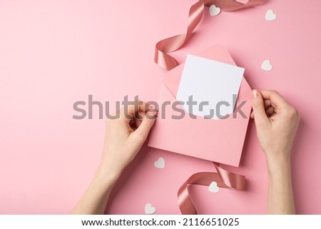 First person top view photo of valentine's day decor girl's hands holding pink envelope with letter heart shaped confetti and pink satin curly ribbon on isolated pastel pink background with copyspace Royalty-Free Stock Photo #2116651025