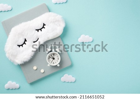 Top view photo of the tender white sleep mask on a grey diary with white small clock and a two pills on it and cute confetti in shape of little clouds on the isolated pastel blue background copyspace