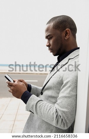Profile portrait African American businessman leaning against wall looking at cellphone