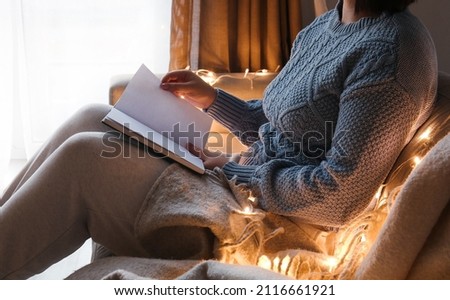 Young woman sitting on sofa and holding opened book with blank pages