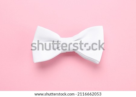 Stylish white bow tie on pink background, top view