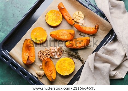 Dish with baked pumpkin pieces on green background