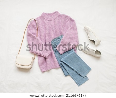 Lilac knitted sweater, blue jeans, white sneakers and bag lie on white background. Overhead view of woman's casual outfit. Trendy stylish women clothes. Flat lay, top view. Royalty-Free Stock Photo #2116676177