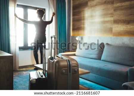 Luggage in modern hotel room with happy young adult female relaxing nearly window, African woman tourist looking to beautiful nature view. Time to travel, relaxation, journey, trip and vacation  Royalty-Free Stock Photo #2116681607