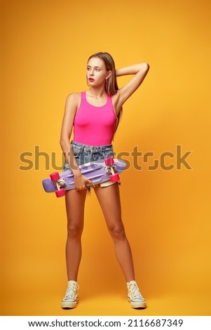Happy summer holidays. Colorful studio portrait of pretty teen girl with skate board on yellow background.