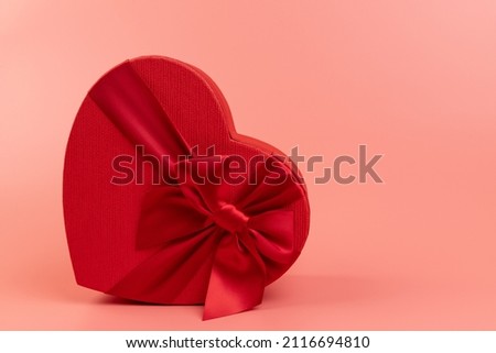 Red heart-shaped gift box with a red ribbon on pink background. Happy Valentine's Day. Anniversary. 