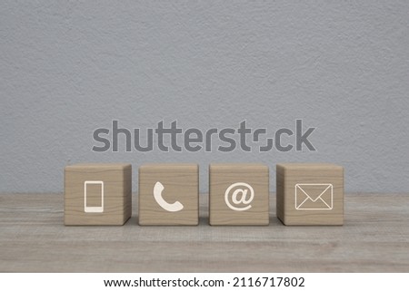 Mobile phone, telephone, email address, mail icon on wood block cubes on wooden table over white wall background, Business customer service and support online concept