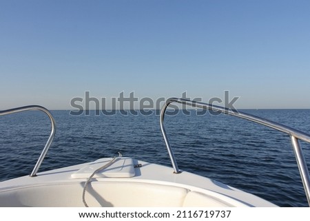A picture of the bow of a motor boat, rushing forward at speed along the sea on a sunny day against the blue sky.