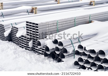 Stainless steel pipes and profiles are stacked, these pipes and profiles are for the food industry, the pipes are covered with snow, winter has come