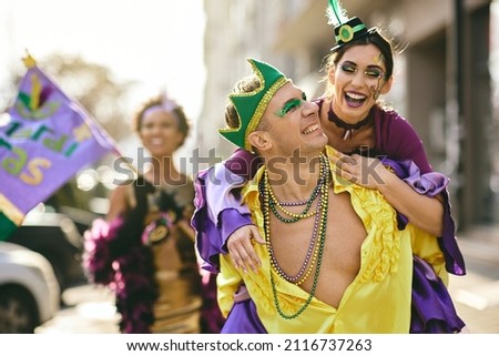Playful couple having fun while piggybacking on street carnival during Mardi Gras celebration.