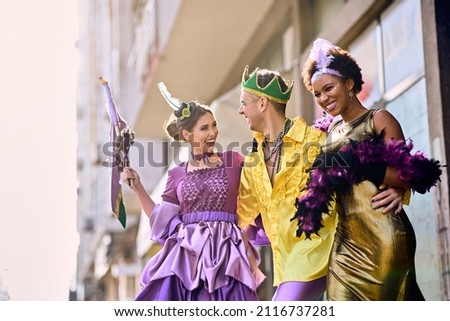 Cheerful group of friends in carnival costumes having fun on the street during Mardi Gras festival.