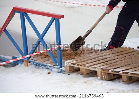 A man pours sand on the slippery wooden pier. Safety preparation for winter swimming sports.