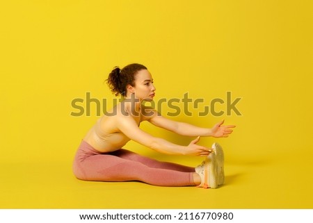 Workout. Young Curly Woman in pink tight sportswear Doing Exercises .Copy Space.studio shot isolated on yellow background