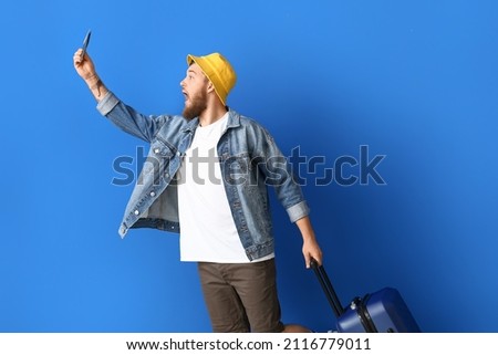 Handsome young man with passport and suitcase on blue background