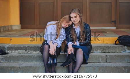 Tired schoolgirls sit barefoot on the steps of the school.