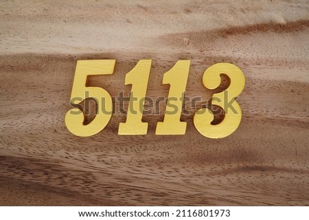 Wooden Arabic numerals 5113 painted in gold on a dark brown and white patterned plank background.