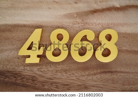 Wooden Arabic numerals 4868 painted in gold on a dark brown and white patterned plank background.