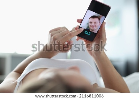 Woman lying in bed and choosing man on dating site using mobile phone closeup