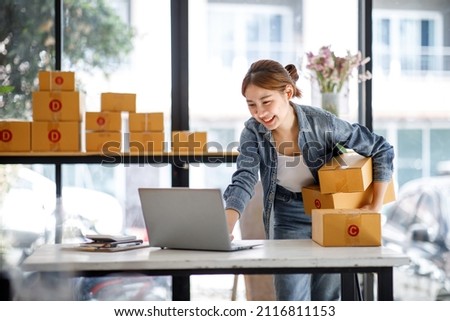 Startup small business entrepreneur or freelance Asian woman using a laptop with box, Young success Asian woman with her hand lift up, online marketing packaging box and delivery, SME concept. Royalty-Free Stock Photo #2116811153