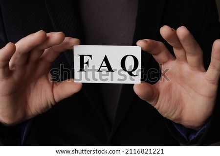 a man wearing a suit sitting in a desk holding a signboard with the word FAQ, Frequently Asked Questions, written in it. High quality photo