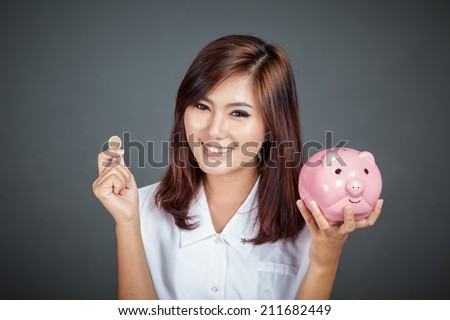 Beautiful Asian girl with a coin and  pink pig money box on gray background