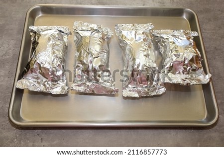 Sweet potatoes wrapped in aluminum paper on a baking pan ready to be put in the oven.