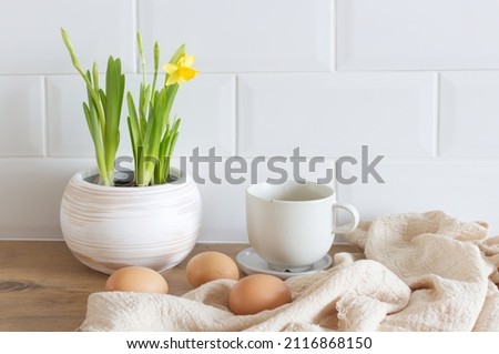 Spring, Easter breakfast still life. A cup of coffee, narcissus, daffodil flowers, hen eggs, and empty picture frame mockups. Linen tablecloth. Farmhouse, Scandinavian interior.        