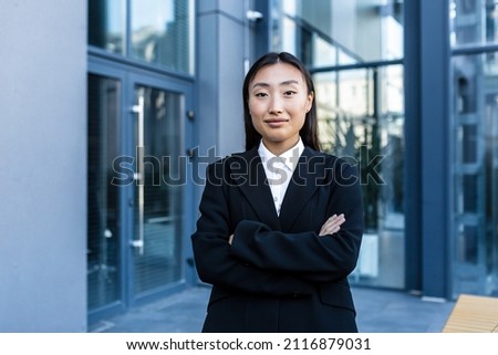 Portrait of successful asian business woman with crossed arms smiling and looking at camera, outside office center
