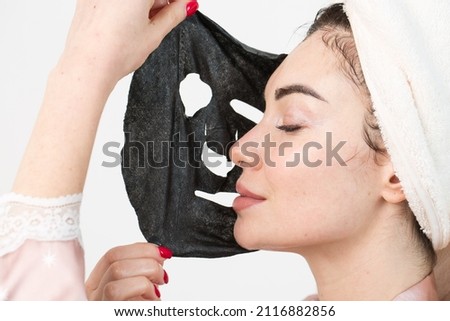Face care and beauty treatments. Woman with a sheet moisturizing mask on her face isolated on white background. Royalty-Free Stock Photo #2116882856