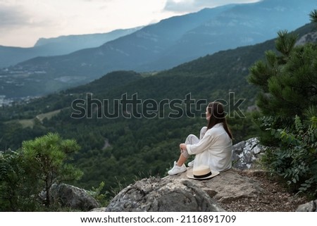 Young beautiful woman with long hair is sitting with her back, meditating and enjoying freedom with a beautiful view of the mountains and the forest. Travel and healthy lifestyle Royalty-Free Stock Photo #2116891709