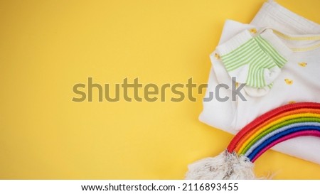 Newborn baby clothes and diy rainbow on yellow background. Baby shower, birthday card with copy space