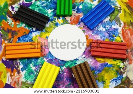 Multi colored rectangle pieces of plasticine, piece of white paper  in the form of a circle lie on a cardboard with plasticine abstract painting, background
