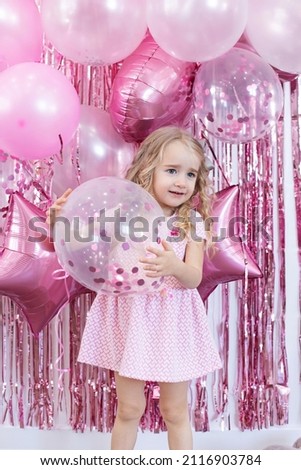 Happy little girl on her 3rd birthday. A girl's birthday, festive decorations, balloons, pink confetti.