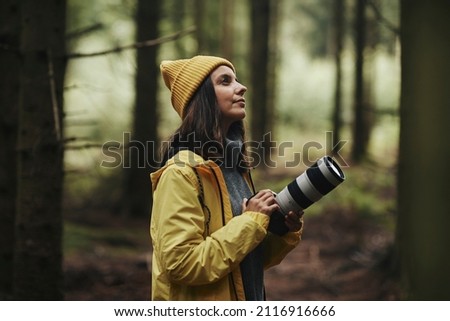 Young woman in outdoor gear taking photos with a telephoto lens during a hike in a forest