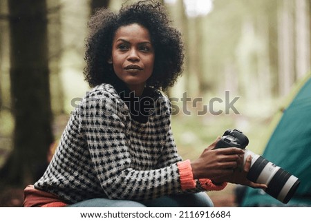 Young African American woman taking photos with a telephoto lens while camping in the woods 