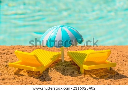 Two yellow toy sun loungers and an umbrella on the beach on a hot day. Relax by the water pool, sea or ocean. Stock photo