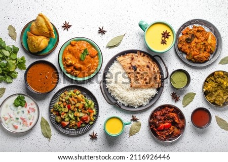 Indian ethnic food buffet on white concrete table from above: curry, samosa, rice biryani, dal, paneer, chapatti, naan, chicken tikka masala, mango lassi, dishes of India for dinner background Royalty-Free Stock Photo #2116926446