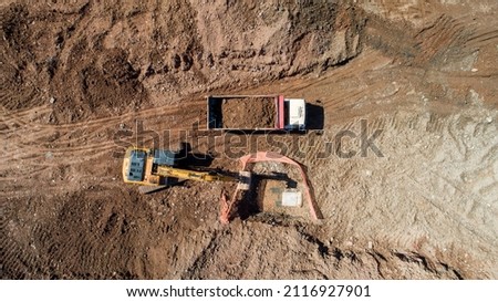 Aerial photo of excavator pours sand into the truck. On construction site top view. Drone shooting. Earthmoving equipment.