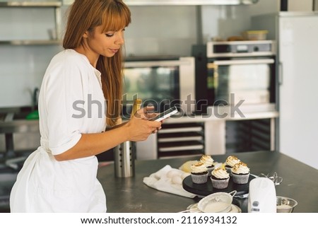 Confectioner girl photographing cupcake for her blog. Girl makes a photo of cupcakes on a smartphone. People using technology.