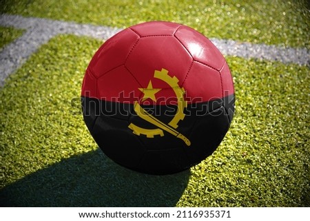 football ball with the national flag of angola lies on the green field near the white line