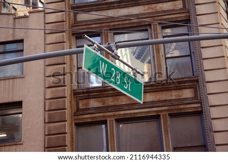 Green big West 28th Street sign hanging on a arch pole in the streets of midtown Manhattan in New York City