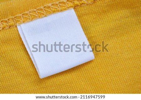 White blank clothing tag label on new yellow shirt background