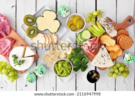 St Patricks Day theme charcuterie table scene against a white wood background. Collection of cheese, meat, fruit and vegetable appetizers. Top down view.